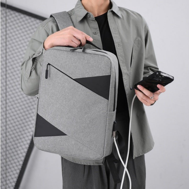 Person holding a gray backpack with geometric design, wearing a light gray shirt and dark pants.