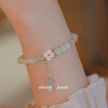 Delicate bracelet with floral charm and gemstone on a wrist, branded 'eleven jewel'.