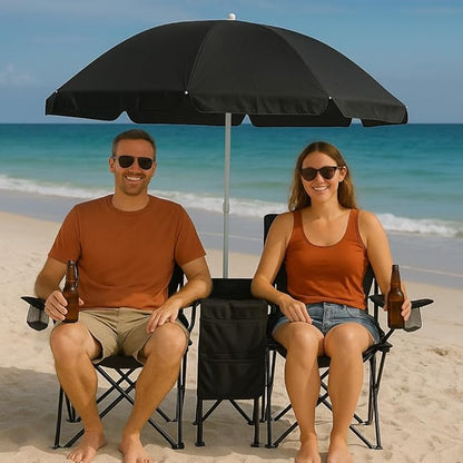 Two people sitting under a black beach umbrella on a sandy beach with ocean in the background.