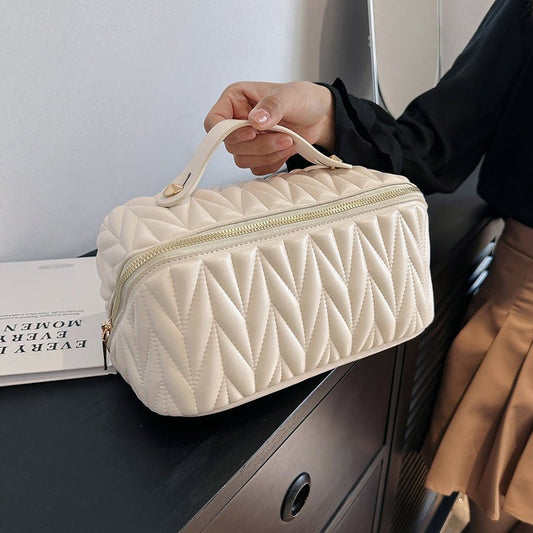 Person holding a quilted beige handbag with a gold zipper.