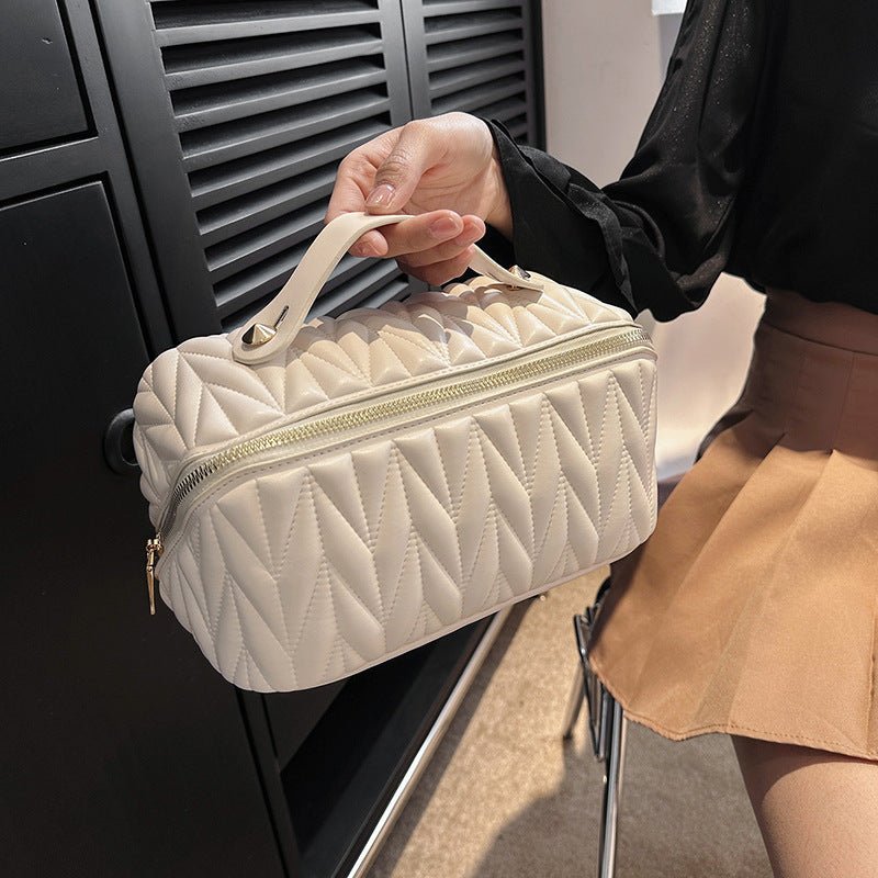 Person holding a quilted beige handbag in front of a black background