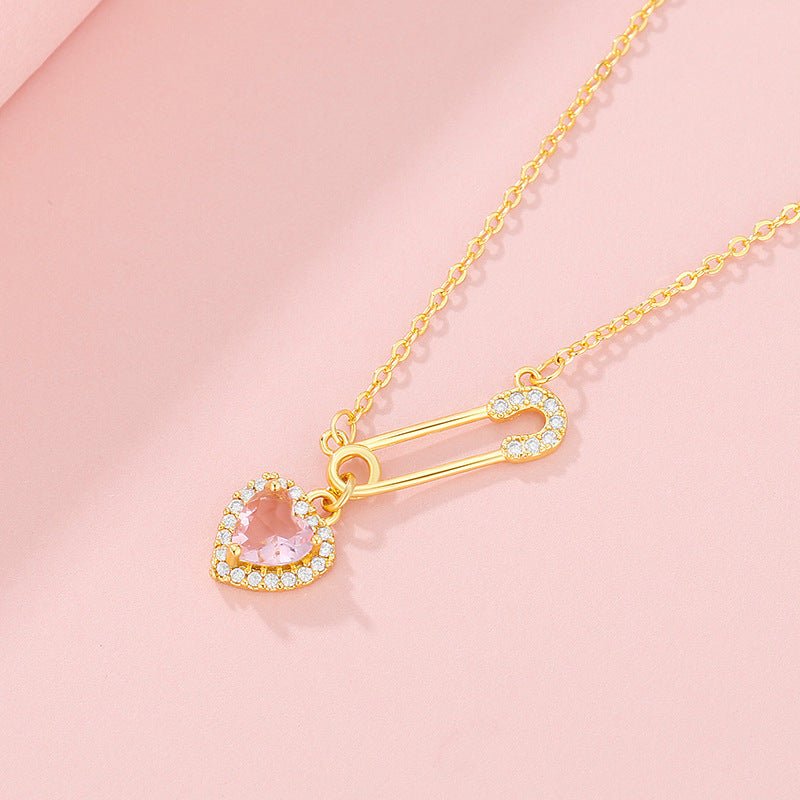 Gold necklace with heart-shaped pink pendant on a pink background