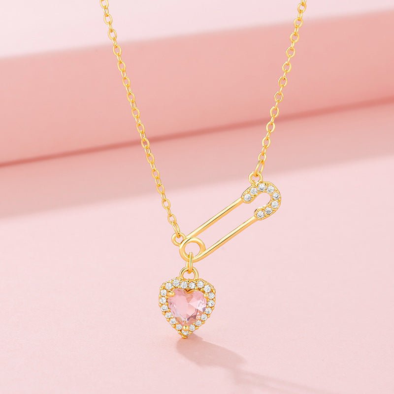 Gold necklace with a heart-shaped pink gemstone pendant on a pink background