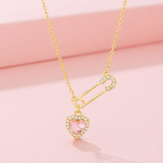 Gold necklace with a heart-shaped pink gemstone pendant on a pink background