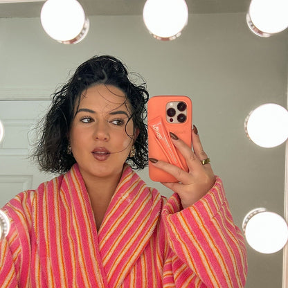 Person wearing a pink and orange striped robe taking a mirror selfie with a phone.