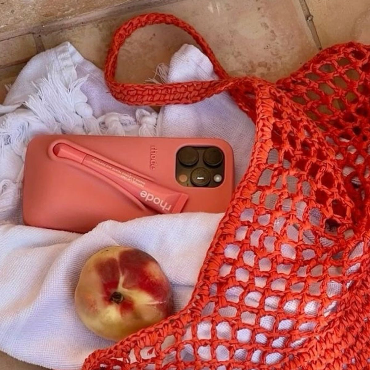 Red woven bag with a peach and pink phone case on a white fabric background