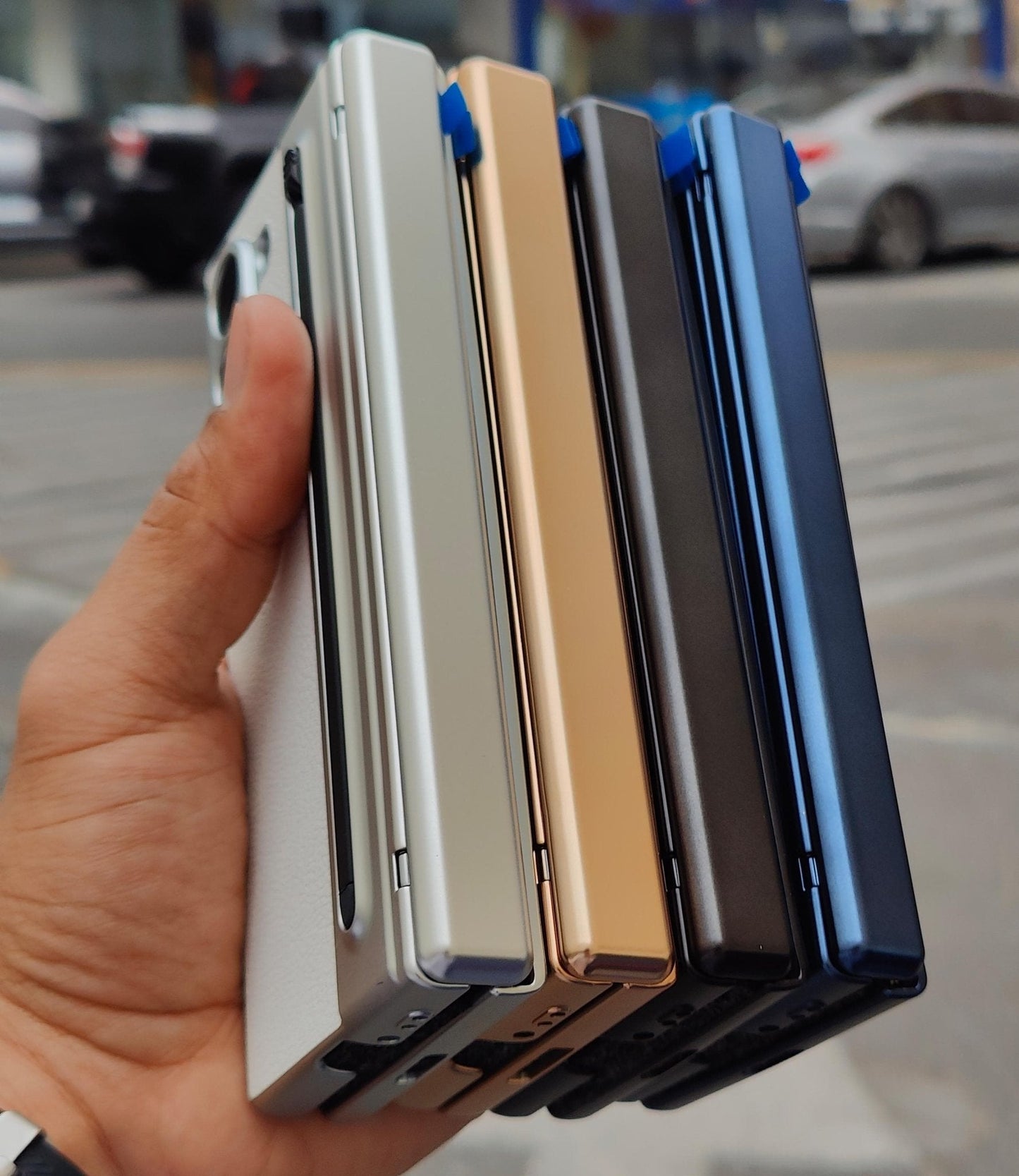 Hand holding four different colored phone cases on a blurred street background