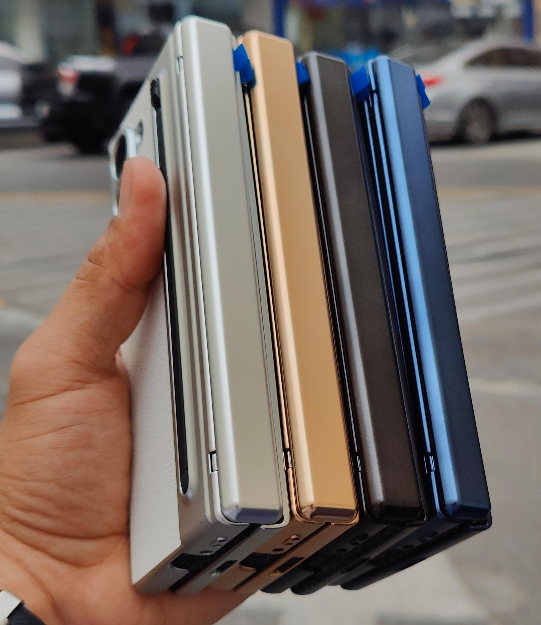 Hand holding four different colored phone cases on a blurred street background