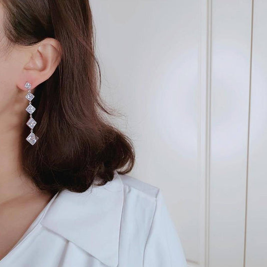 Close-up of a person wearing diamond earrings with a neutral background
