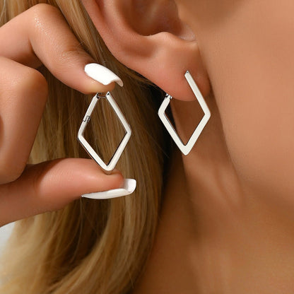 Close-up of a person wearing geometric hoop earrings with a hand adjusting one.