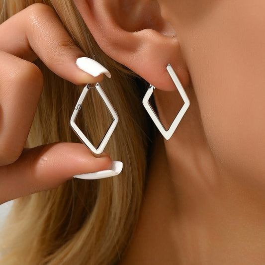 Close-up of a person wearing geometric hoop earrings with a hand adjusting one.