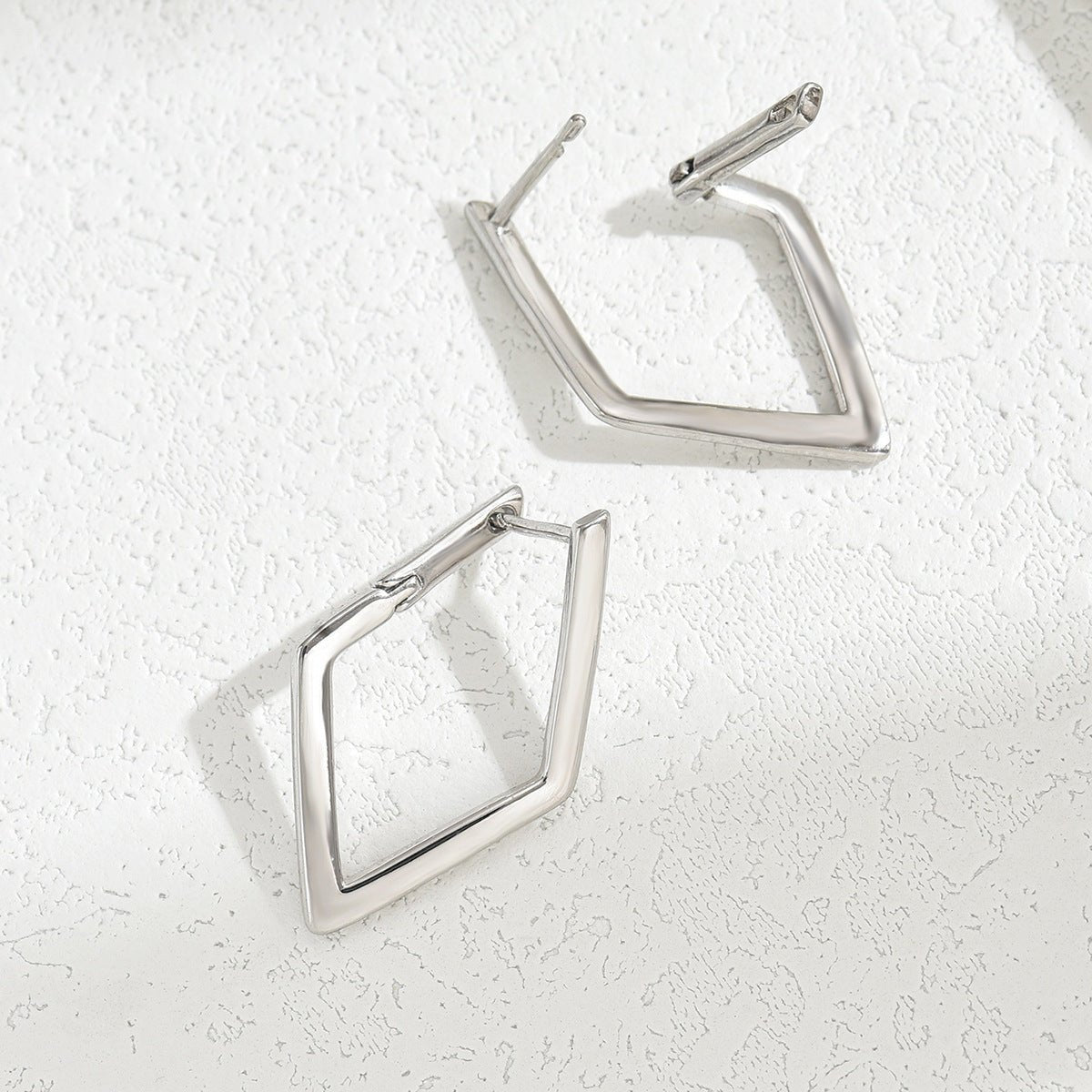 Silver geometric hoop earrings on a textured white surface