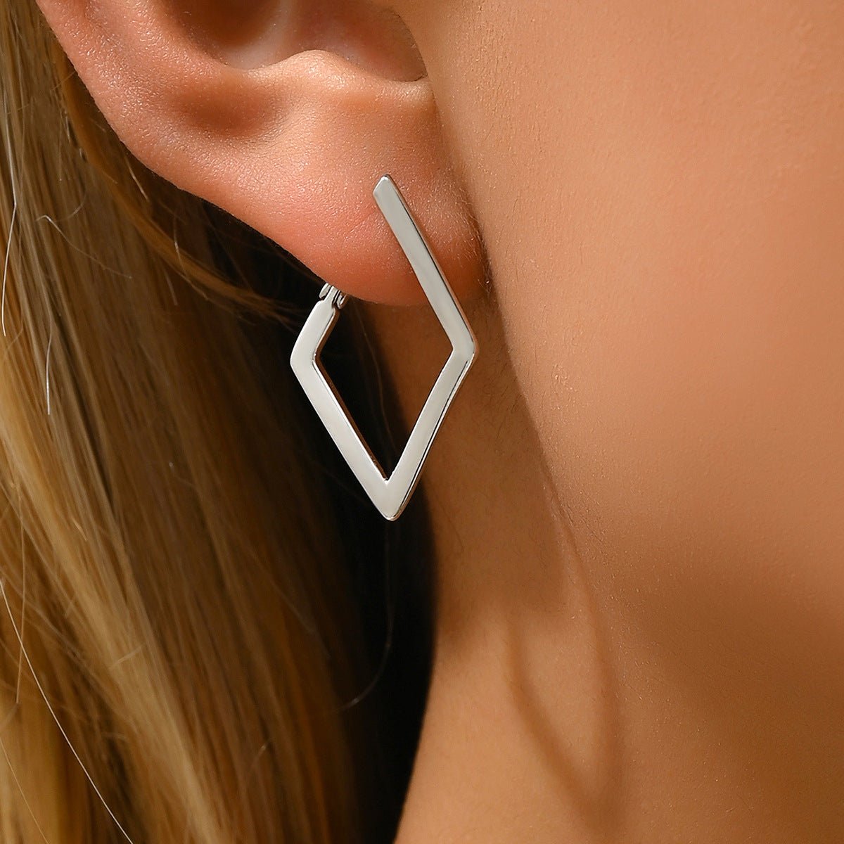 Silver geometric hoop earring worn by a person with blonde hair.