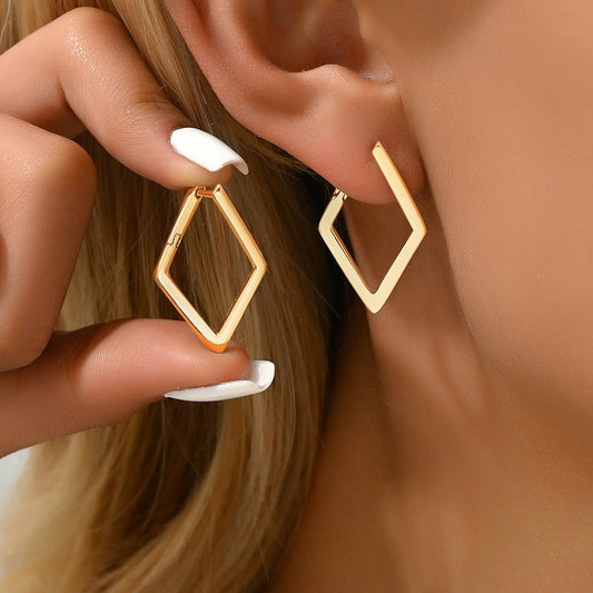 Gold hoop earrings being worn and held by a hand with white nail polish.