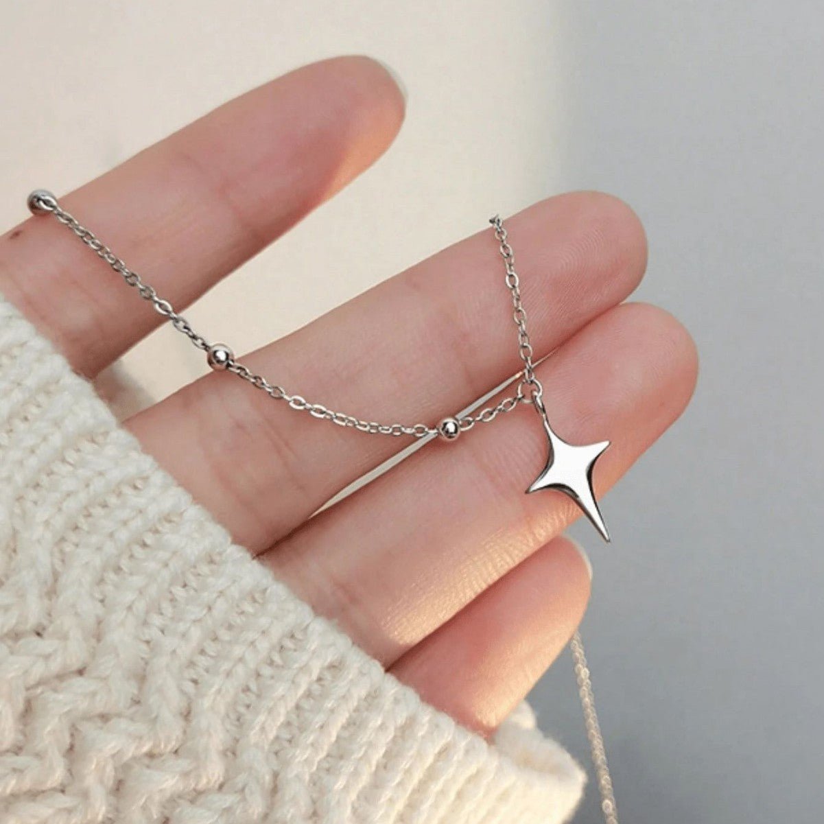 Silver star necklace on a hand with a neutral background