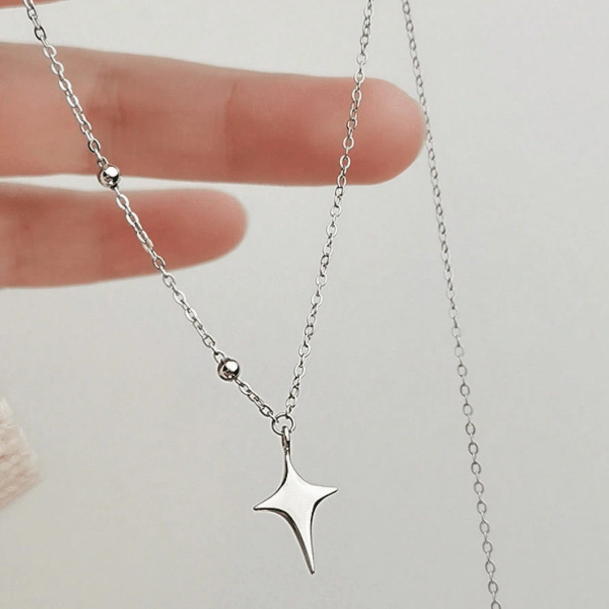 Silver star necklace held by a hand on a light background