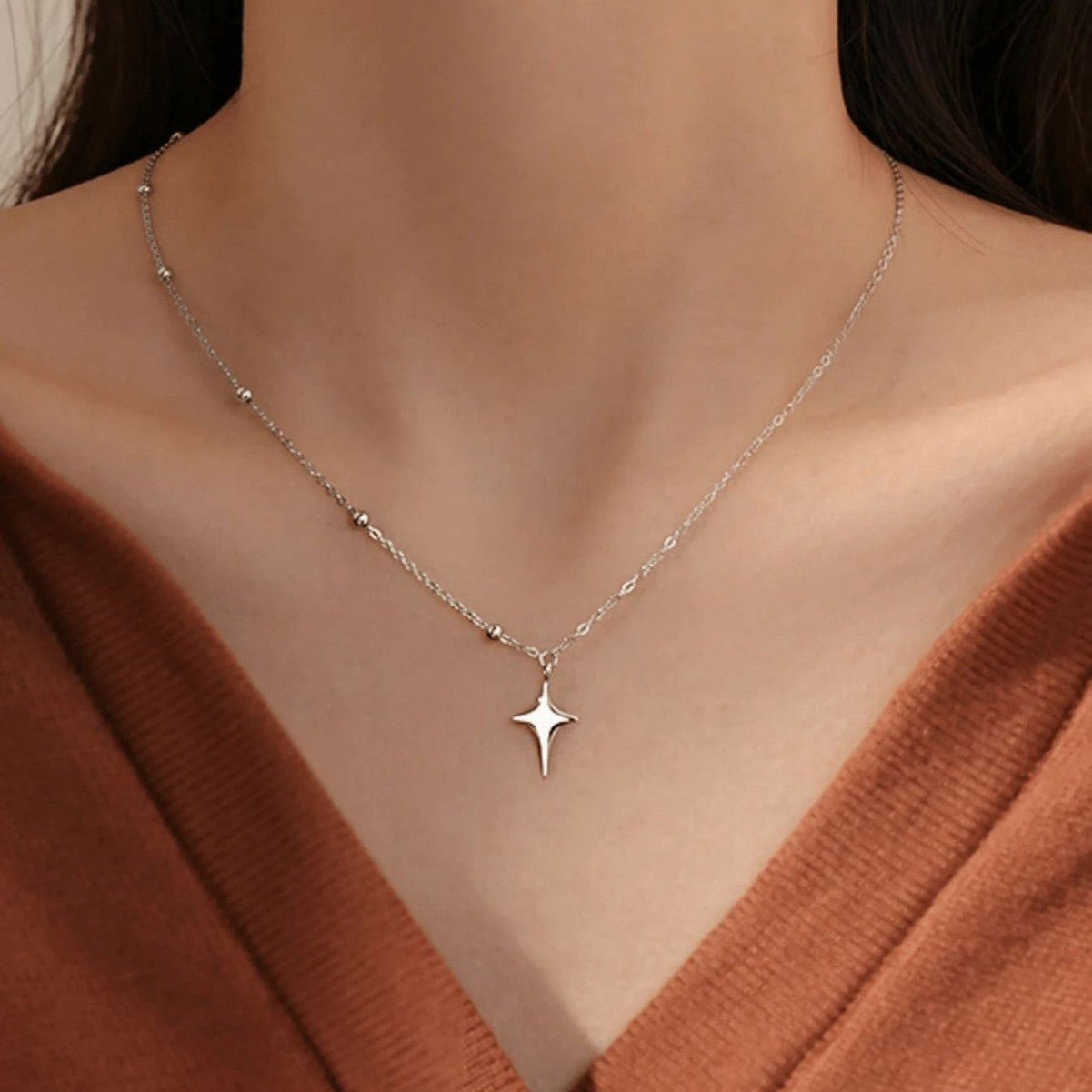 Silver star-shaped necklace on a model wearing a rust-colored top