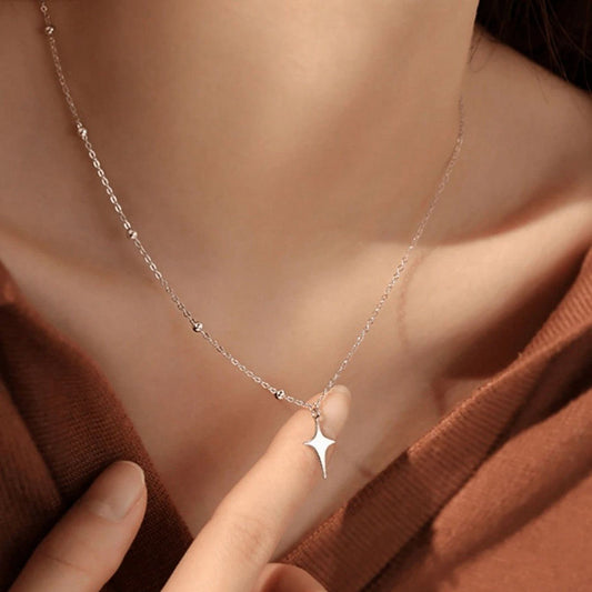 Star-shaped pendant on a delicate chain worn by a person against a brown background