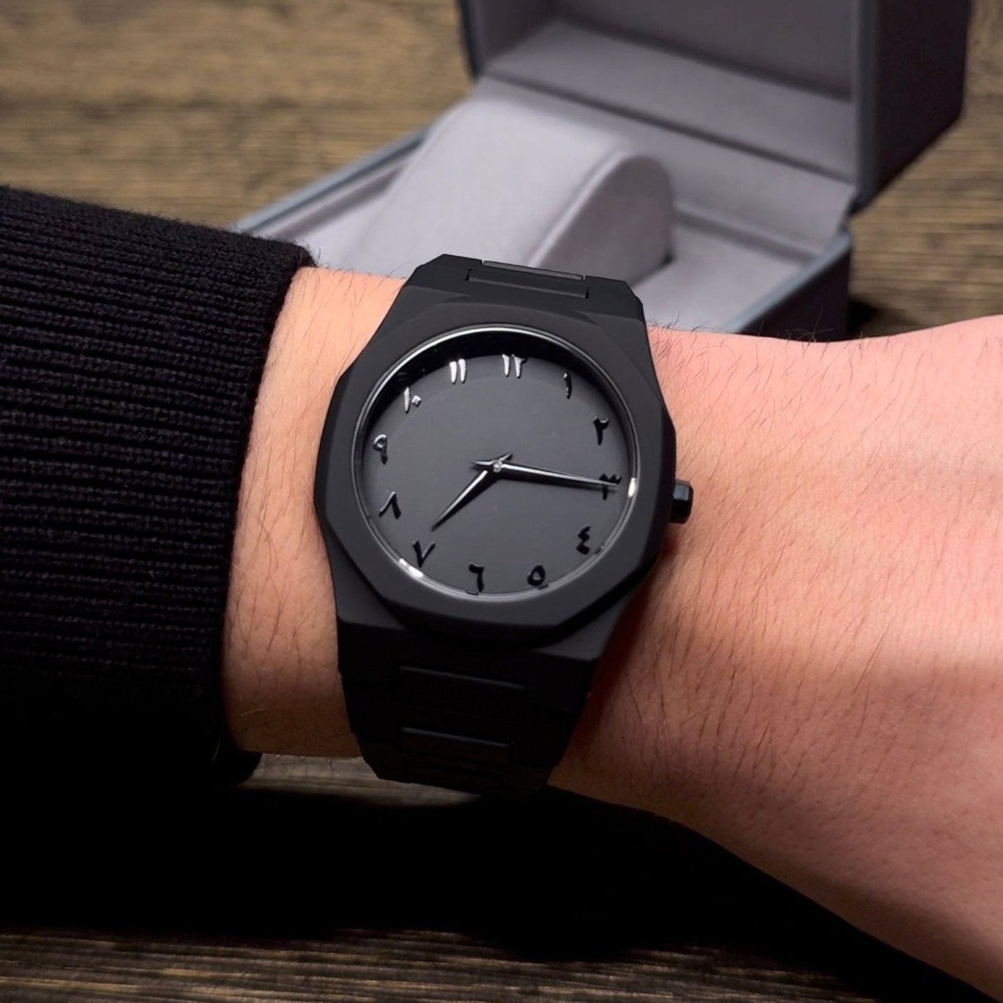 Black watch on a wrist with a wooden surface and gray box in the background