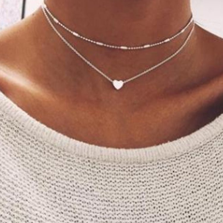 Silver heart-shaped necklace on a person wearing a light gray sweater.