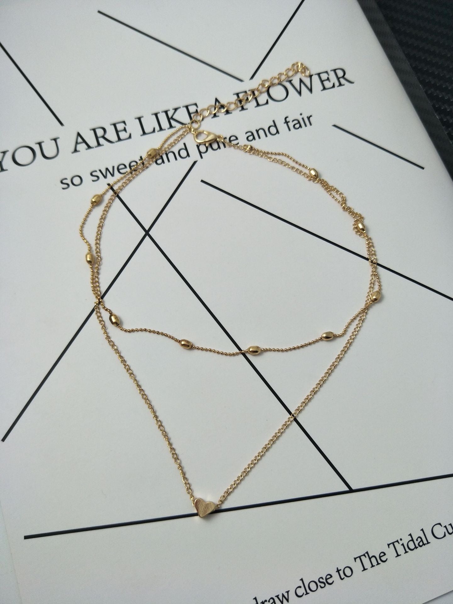 Gold necklace with heart pendant on a printed paper background