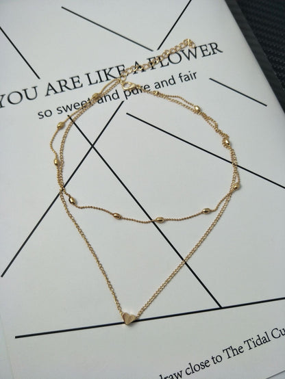 Gold necklace with heart pendant on a printed paper background